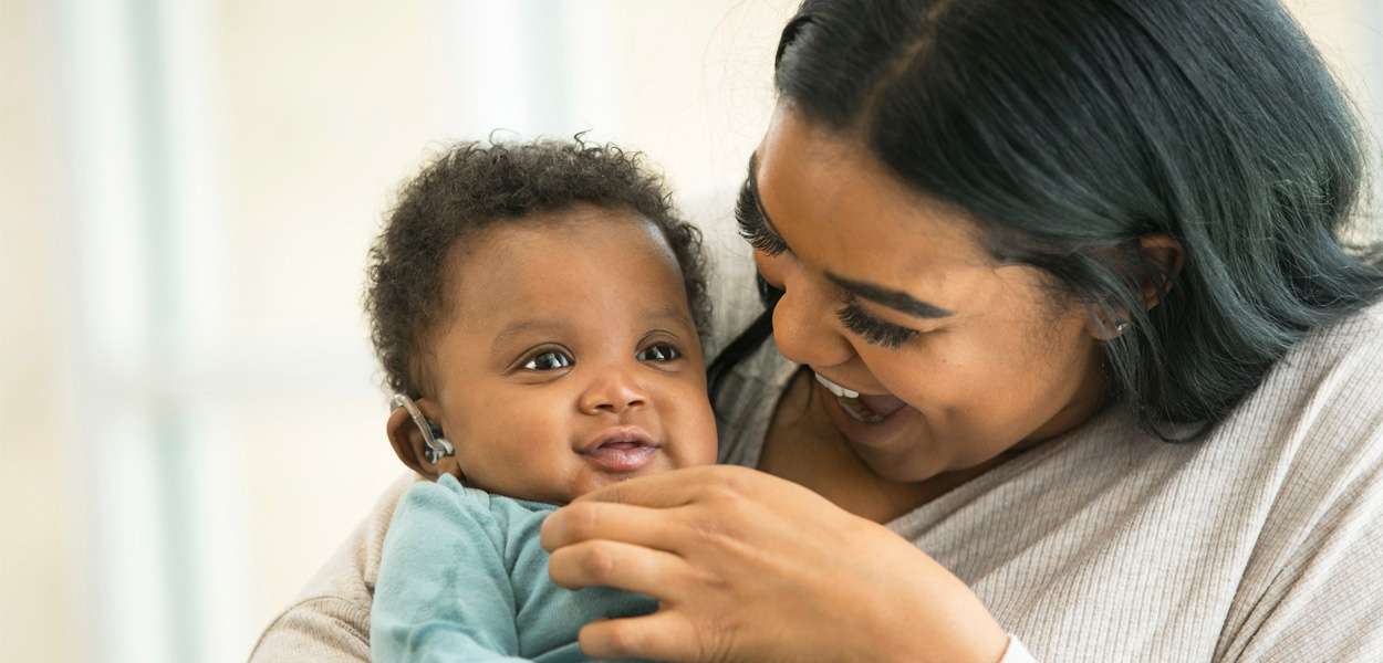 An excited adult holding an infant wearing hearing aids